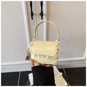 Détail d'un sac à main jaune à pois bleus avec bordure en dentelle et pompon en peluche