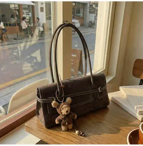 Detail of dark brown suede handbag featuring silver buckles and plush bear charm decoration