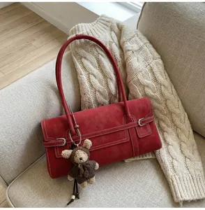 Detail of red suede shoulder bag with bear pendant on a cozy beige sweater background