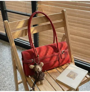 Detail of red suede shoulder bag with contrast white stitching and cute teddy bear charm