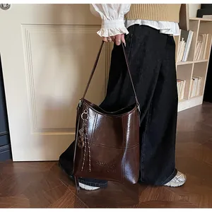 Detail der braunen Vintage-Beuteltasche mit Logo-Prägung und dekorativem Quastenanhänger