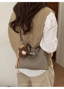 Close-up of grey leather bucket bag with silver clasp and plush bear charm on model