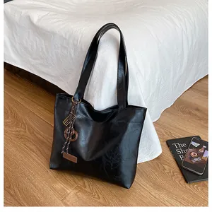 Détail d'un cabas noir brillant en cuir avec pendentif tressé et livre en arrière-plan
