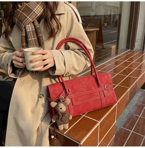 Detail of brick red faux leather shoulder bag featuring a cute bear plush keychain