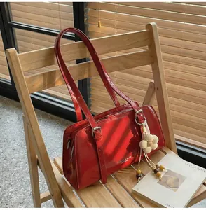 Close-up of glossy red faux leather shoulder bag with floral pendant on a wooden chair