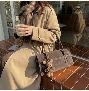 Detail of vintage brown suede shoulder bag with decorative bear plush charm in autumn setting