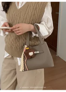 Detail of dark taupe lychee leather handbag featuring silver twist lock and bear charm