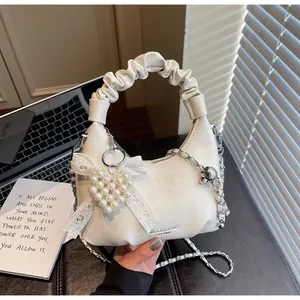 Detail of a creamy white pleated handbag with pearl heart charm and lace bow decor