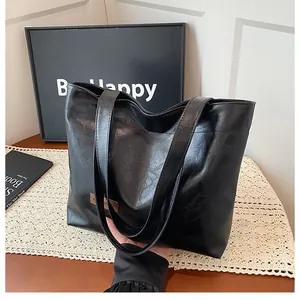 Détail d'un sac cabas noir en similicuir texturé avec un écusson rectangulaire marron