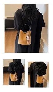 Detail view of yellow suede bucket bag with black top handle and bunny charm accessory