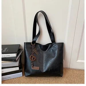 Détail du sac cabas en cuir noir texturé avec étiquette mode et charm nœud marron