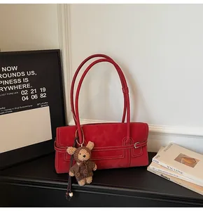 Detail of red faux suede shoulder bag with white stitching and plush bear charm