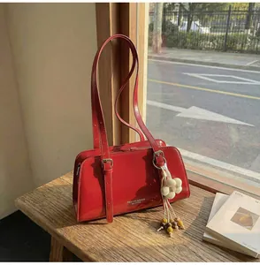 Close-up of a glossy red shoulder bag with floral pendant and polished leather texture