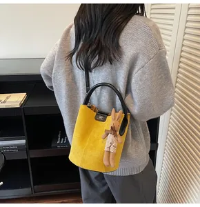 Yellow suede bucket bag detail with black handle and cute rabbit charm on a grey sweater