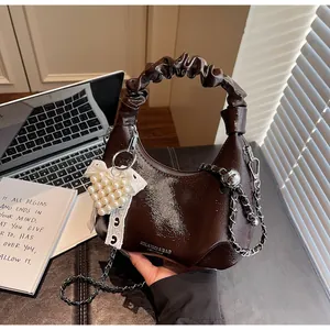 Detail of dark brown glossy hobo bag with pearl heart charm and silver chain strap