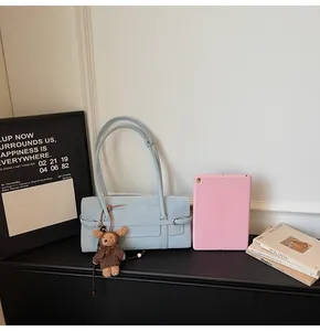 Light blue shoulder bag with brown plush bear charm in a stylish lifestyle home setting
