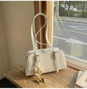 Detail of cream white patent leather shoulder bag with floral charm on wooden table