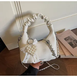 Detail of white pleated handbag featuring heart pearl charm and delicate lace bow