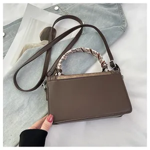 Brown leather crossbody bag with silk scarf wrapped handle on lifestyle background