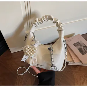Detail of a creamy white pleated hobo bag with pearl heart charm and lace bow decor