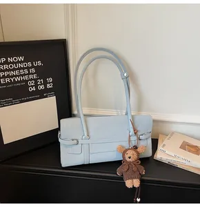 Detail of light blue rectangle shoulder bag with cute brown plush bear charm and sleek strap
