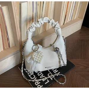 Close-up of pleated cream handbag with pearl heart charm and metal chain on vintage books