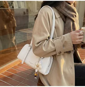Close-up of white leather underarm bag with decorative floral pendant and logo text