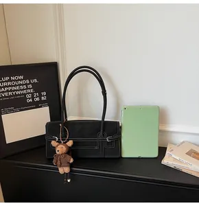 Detail of black rectangular shoulder bag with white contrast stitching and teddy bear charm