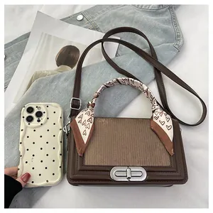 Detail of a brown leather and fabric handbag with a silk scarf tied on the handle