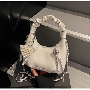 Detail of a creamy white pleated hobo bag with a pearl heart charm on a black step background