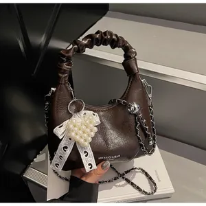 Detail of a brown pleated handbag with pearl heart charm and metallic chain strap