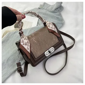 Close-up of brown textured crossbody bag with silver lock and heart print scarf
