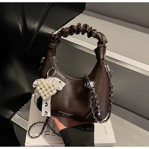 Detail of a dark brown glossy handbag with a ruched handle and pearl heart charm