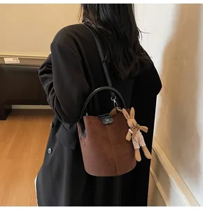 Detail of brown frosted leather bucket bag with plush rabbit charm and gold hardware