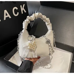 Detail of off-white pleated leather handbag featuring pearl heart charm and silver chain
