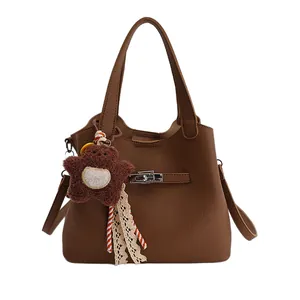 Brown lychee grain bucket bag with silver twist lock and plush bear charm on white background