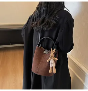 Detail of brown suede bucket bag with round handles and a cute bunny plush charm