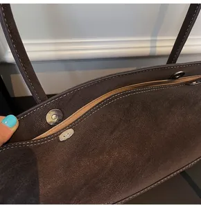 Detail view of dark brown tote bag showing magnetic snap closure and white contrast stitching