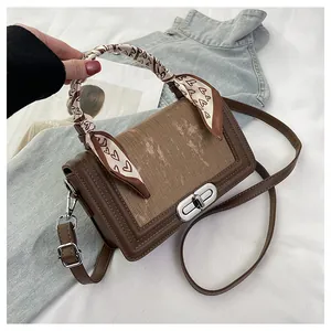 Detail of a brown leather crossbody bag with heart pattern scarf and silver clasp lock