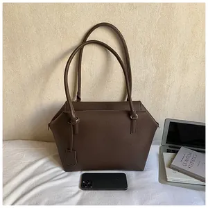 Gros plan sur la texture cuir litchi marron foncé et doubles anses du sac cabas