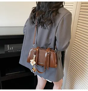 Brown leather tote bag featuring a white flower charm and adjustable shoulder strap