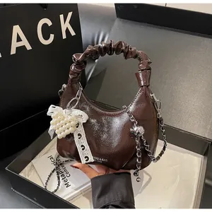 Detail of dark brown glossy crossbody bag with pearl bow and silver chain in a gift box