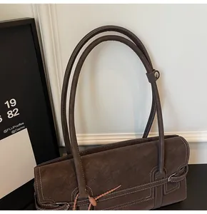 Detail view of dark brown suede shoulder bag with white contrast stitching and side buckles
