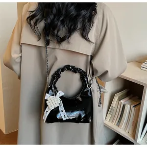 Detail of a shiny black patent leather mini bag with pearl heart charm and metal chain