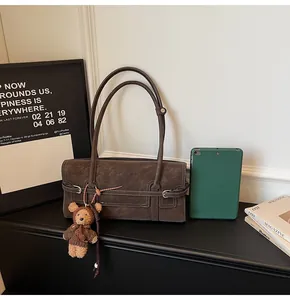 Detail of vintage brown tote bag featuring decorative stitching and a plush bear pendant