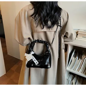 Detail view of black patent leather crossbody bag with pleated handle and pearl bow charm