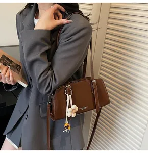 Detail of a brown leather tote bag featuring a white flower charm and brand lettering