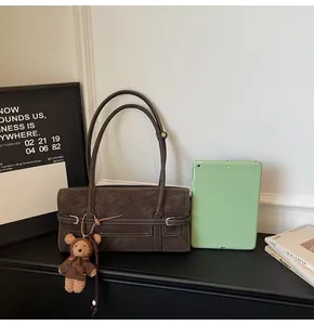 Detail of dark brown faux suede shoulder bag with decorative strap and plush bear charm