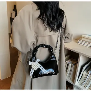 Detail of black glossy bag with pleated handle, pearl heart charm and lace ribbon