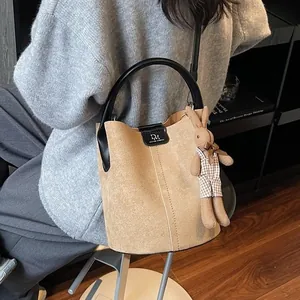Brown suede bucket bag with black top handle and cute rabbit charm in indoor setting